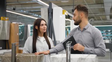 Profesyonel erkek danışman, genç bir bayan müşteriye banyo için yeni bir lavabo seçmesinde yardımcı olurken, başarılı bir satın alma sonrasında çift el sıkışıyor.
