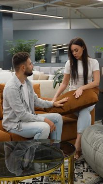 Geniş, modern bir mobilya galerisinde yan yana otururken iç dekoratif yastıklı yeni bir kanepeyi tartışan ve seçen pozitif genç bir çift.