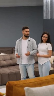 Mobilya mağazasında yürüyen mutlu beyaz bir çift evleri için aktif olarak yeni bir kanepe seçiyor ve tartışıyor, ortak kararları ve ev gelişimini simgeliyor.