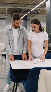 Genç evli bir çift modern bir mobilya mağazasında yeni bir yemek masası seçiyor, mermer yüzeye dokunuyor ve çağdaş ev dekorasyonu seçimlerini tartışıyorlar.