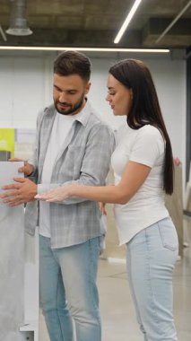Yeni seramik fayansları ev yenileme projeleri için tartışan ve seçen pozitif genç çift, büyük bir modern hırdavat mağazasında veya özel sergi salonunda birlikte mutlu bir şekilde alışveriş yapıyorlar.
