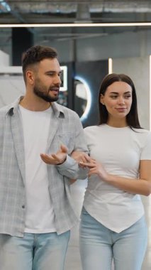 Neşeli genç bir çift modern bir ev geliştirme mağazasında birlikte yürüyor, evleri için yeni mobilyalar tartışıyor ve seçiyorlar, ortak yaşam alanları için mutlu kararlar alıyorlar.