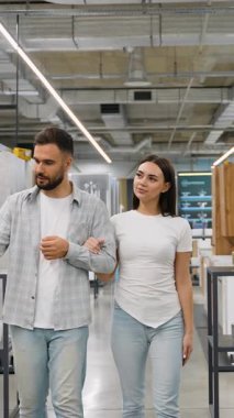 Mutlu genç çift ev dekorasyonu mağazasında el ele yürüyorlar. Ev yenileme projeleri için yeni banyo armatürleri ve fayanslar seçip tartışıyorlar.