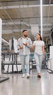 Mutlu genç bir çift birlikte bir ev geliştirme mağazasında yürüyorlar, banyo yenilemeleri için yeni hijyenik eşyalar seçiyorlar ve lavabo ve musluklara bakarken alışverişlerini tartışıyorlar.
