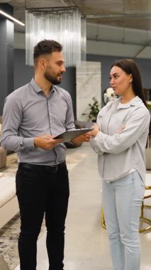 Bir kadın müşteriyle konuşan profesyonel bir satıcı, seçenekleri tartışıyor ve modern, zarif bir mobilya mağazasında dururken uzman tavsiyesi veriyor.