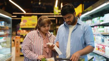 Genç Hintli çift, uzun bir kağıt makbuzunu kontrol ederken ve süpermarket koridorundaki harcamaları hesaplarken şaşkın ve endişeli hissediyorlar. Mali kriz ve artan gıda fiyatları kavramı