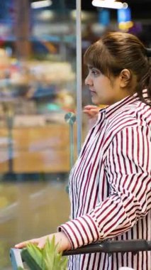 Alışveriş arabalı genç Hintli kadın marketteki soğutuculu vitrinden taze bıldırcın yumurtası seçiyor, ailesine yiyecek almadan önce paketi dikkatlice inceliyor.