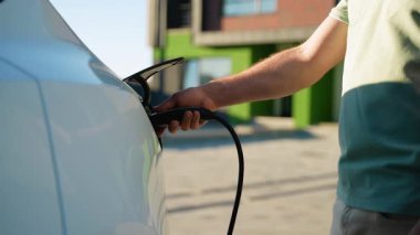 Daha yeşil bir gelecek için sürdürülebilir ulaşım ve temiz enerjiyi teşvik eden, modern elektrikli araçlardan şarj aletinin bağlantısını kesen bir erkeğin yakın görüntüsü
