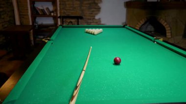 Profesyonel oyuncu, Rus piramit bilardo oyununda kırmızı bilardo topuna nişan alıp, onu yeşil keçeli masa üzerine kurulmuş beyaz toplara doğru gönderiyor.