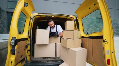 Üniformalı bir teslimatçı, karton kutularla dolu sarı bir minibüsün arkasında dikilirken dosyasını kontrol ediyor, sevkiyatları yönetiyor ve eksiksiz bir siparişin yerine getirilmesini sağlıyor.