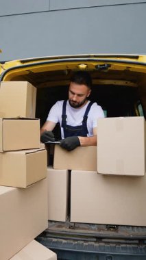 Tulum giymiş bir teslimatçı gülümsemeden önce karton kutularla dolu bir kargo aracının arkasında envanter listesini kontrol ediyor.