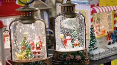 Kadınlar el pençe divan bir mağazadan kardan adam sahnesiyle bir kar küresi feneri seçiyor, Noel Baba küresi gibi diğer Noel süsleriyle çevrili, tatil sezonuna hazırlanıyor.