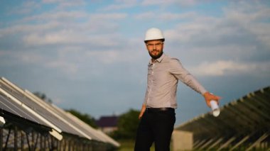 Bir güneş paneli elektrik santralinin planıyla başarıyı kutlayan sert şapkalı neşeli yenilenebilir enerji mühendisi yeşil elektrik üretiminden memnun olduğunu gösteriyor.