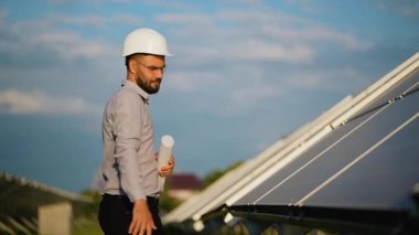 Bir güneş paneli elektrik santralinin planıyla mutlu bir şekilde dans ederek başarıyı kutlayan sert şapkalı neşeli yenilenebilir enerji mühendisi..
