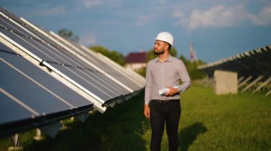 Bir elektrik santralindeki güneş panellerini incelerken elinde planları olan erkek mühendis, yeşil bir gelecek ve çevresel bakım için yenilenebilir ve sürdürülebilir enerji üretimine odaklandı