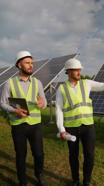 İki erkek mühendis bir güneş çiftliğinde yürürken, biri dizüstü bilgisayar, diğeri ise fotovoltaik dizilimle bir plan taşıyor.