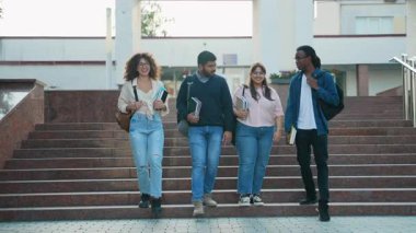 Dersten sonra merdivenlerden inip sırt çantalarını ve kitaplarını taşıyan ve ağır çekimde gülümseyen çok ırklı bir arkadaş grubu.