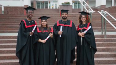 Mezuniyet töreninden sonra mutlu mesut gülümseyen ve diplomalarını gösteren, akademik başarılarını kutlayan akademik önlüklü ve şapkalı gururlu öğrenciler.