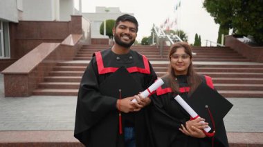 İki gururlu Hintli yüksek lisans öğrencisi ellerinde diplomalar ve kameraya gülümseyerek üniversite kampüsünün merdivenlerinde mezuniyet törenindeki başarılarını kutluyorlar.