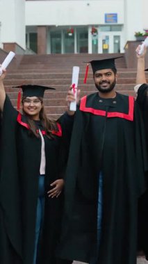 Siyahlar içinde gururlu Hint üniversitesi mezunları akademik başarılarını kutlamak için kampüs binası önünde diplomalarını yükselterek başarıyı ve parlak geleceği sembolize ediyorlar.