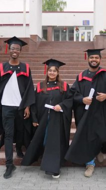 Siyahi akademik önlükler ve şapkalar içinde gururlu çok uluslu mezunlar üniversite binasının merdivenlerinden neşeyle iniyorlar, akademik başarılarını ellerinde diplomalarla kutluyorlar.
