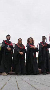 Diplomalarını kampüste tutarken akademik başarılarını kutlamak için şapkalarını havaya fırlatan üniversite öğrencilerinden oluşan mutlu bir grup.