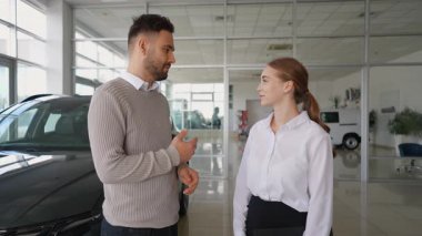 Professional female car dealer smiling while handing over the keys and shaking hands with a happy male customer after a successful purchase agreement
