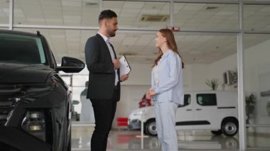 Genç bir kadın galeride yeni bir araba alıyor, satış müdüründen anahtarları alıyor, ve başarılı bir anlaşma yapmak için el sıkışıyor, modern bir araç satın almaktan mutlu oluyor.