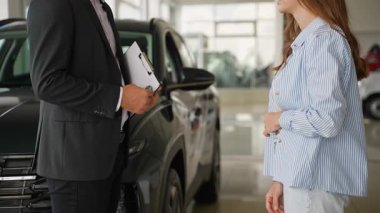 Tanınmayan bir erkek araba satıcısı başarılı bir araç satın alma anlaşmasından sonra anahtarları veriyor ve mutlu bir kadın müşteriyle el sıkışıyor.