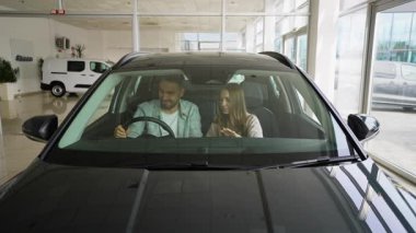 Genç bir adam ve bir kadın yepyeni siyah bir arabanın içinde oturmuş, onun özelliklerini ve içini büyük bir hevesle tartışıyorlar. Mutlu bir aile, galeriden bir araç alıyor ve önemli bir karar veriyor.