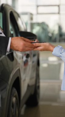 Profesyonel araba satıcısı yeni bir otomobilin anahtarlarını teslim ederek ve bayan müşteriyle el sıkışarak anlaşmayı tamamlıyor. Galeride başarılı bir satın alımı kutluyor.