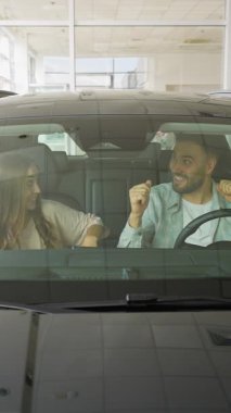 Genç, neşeli bir çift, galeride arabanın içinde otururken dans ederek ve şarkı söyleyerek yeni arabalarının satın alınmasını kutluyor. Yeni arabaları için mutlu ve heyecanlılar.