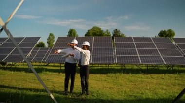 Güneş çiftliğinde yürürken fotovoltaik paneller ve yenilenebilir enerji projesini tartışan iki çok ırklı mühendis.