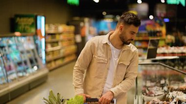 Genç bekar, marketin koridorunda alışveriş arabasını itiyor. Buzdolabından bir paket tütsülenmiş et seçiyor.