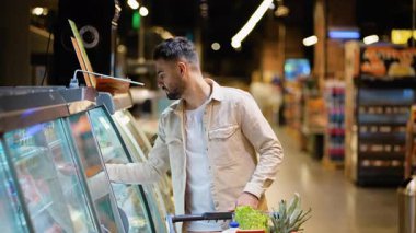 Markette alışveriş yapan genç bir bekar, sağlıklı bir yemek için soğutulmuş bölümden taze somon filetosu seçiyor.