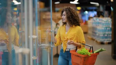 Kıvırcık saçlı çekici bir kadın mandıra reyonundaki dondurulmuş vitrinden bir kutu yumurta topluyor.
