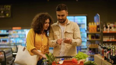 Marketten taze yiyecek alırken alışveriş listesi okuyan mutlu çift. Erkek ve kadın süpermarket koridorunda ürünleri kontrol ediyorlar.
