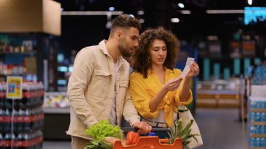 Bir süpermarket koridorunda yüksek fiyatları tartışan genç bir aile. Finansal stres ve aşırı harcama kavramı