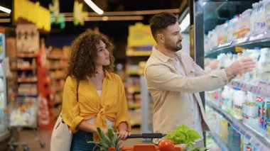 Süpermarketten alışveriş yapan mutlu genç çift. Erkek ve kadın süt ürünlerini seçiyor ve süt şişesindeki etiketi okuyor.