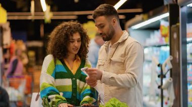Genç evli çift alışveriş listelerini dikkatlice kontrol ediyor. Karı koca birlikte bütçe ve tercihlerini tartışıyor.