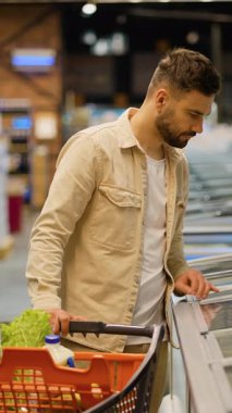 Alışveriş arabalı beyaz bir adam marketteki buzdolabından taze donmuş balık seçiyor. Sağlıklı gıda ürünleri satın alıyor.