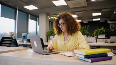 Yoğunlaşmış genç bir kadın üniversite sınıfında okuyor, materyalleri gözden geçiriyor ve sakin bir akademik ortamda sınavlara hazırlanıyor