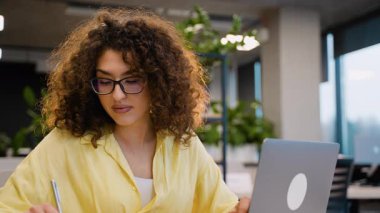 Kıvırcık saçlı, gözlüklü ve modern bir sınıfta notlar yazan çekici bir genç öğrenci. İşinden başını kaldırıp gülümsüyor.