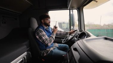 Profesyonel erkek sürücü kamyonun direksiyonunda oturuyor ve telsizle konuşuyor. Modern lojistik ve nakliye konsepti
