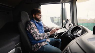 Kabinde oturan odaklanmış kamyon şoförü, dizüstü bilgisayarı üzerinde çalışıyor direksiyona yerleştiriliyor, lojistik ve planlama rotalarını yönetiyor.