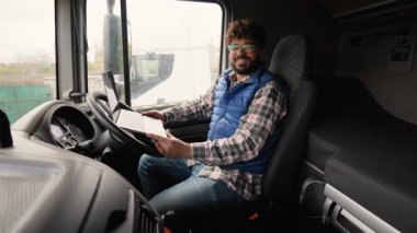 Bir kamyon kulübesinin içinde dizüstü bilgisayarda çalışan genç bir adam. Yolculuktan önce lojistik yönetimi için bilgisayar kullanan profesyonel erkek sürücü