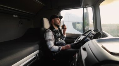 Kamyon kabininde oturan kendine güvenen erkek sürücü iletişim için telsiz kullanıyor. Nakliye ve lojistik sektörü kavramı