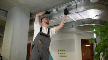 Ofis tadilatı sırasında kablosuz tornavida kullanarak metal kablo tepsisine bağlantı kutusu yerleştiren profesyonel elektrikçi.