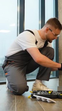 İş tulumları ve güvenlik gözlükleri üzerine odaklanmış elektrikçi modern bir ofiste beton bir duvara yeni bir elektrik prizi yerleştiriyor.