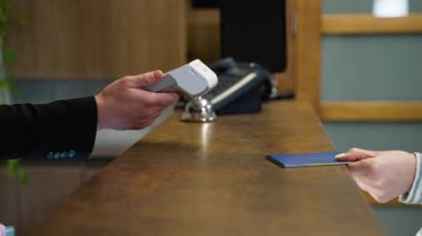 Otel kasasında kredi kartıyla temas kurmadan ödeme yapan bir konuğun fotoğrafını çek. Resepsiyonist işlemler için posizyon terminalini tutuyor.